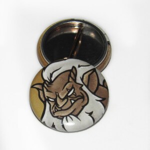 May include: A round button with a cartoon illustration of a brown, white, and black gargoyle with an angry expression. The button is on a white background, with a second button showing the pin back.