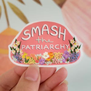 May include: Pink sticker with the text "SMASH the PATRIARCHY" in white lettering. The sticker is decorated with a border of colorful flowers.