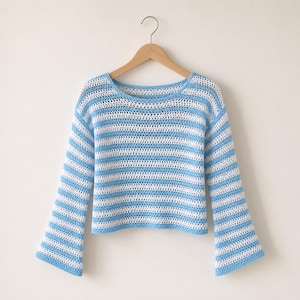 May include: A blue and white striped crochet sweater with long sleeves hangs on a wooden hanger. The sweater features a round neckline and a cropped length. The blue and white stripes are horizontal and evenly spaced.