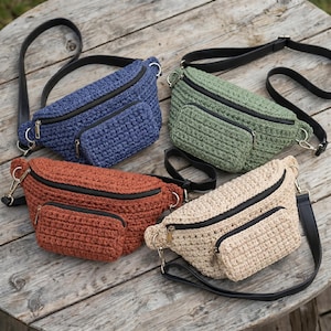 Peut inclure: Quatre sacs banane en crochet bleus, verts, rouille et beiges. Chaque sac a un compartiment principal zippé et une petite poche avant, tous avec des fermetures éclair noires. Ils ont des sangles réglables noires et des accessoires argentés.