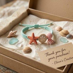 May include: A light blue woven bracelet featuring a crocheted orange starfish, a beige sand dollar, and a pink jellyfish charm. The bracelet is presented in a cardboard box with seashells, sea glass, and a note reading Thank you for your purchase!