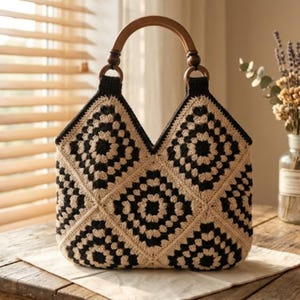 May include: A crochet handbag featuring a black and beige granny square pattern. The bag has a V-shaped top opening and two rounded wooden handles attached with dark crochet loops. The structure is composed of multiple square motifs joined together.