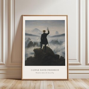 May include: A framed art print featuring a parody of Caspar David Friedrich's Wanderer above the Sea of Fog, showing a figure in a dark coat standing on a rocky cliff holding a smartphone, with the text CASPAR DAVID FRIEDRICH Wanderer above the Sea of Fog.