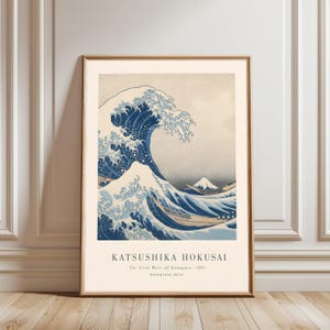 May include: Framed print of Katsushika Hokusai's "The Great Wave off Kanagawa." The artwork depicts a large, stylized wave in shades of blue, with a view of Mount Fuji in the background. The print includes the title and artist's name.