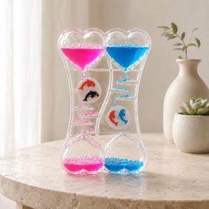 Peut inclure: Un bulleur à mouvement liquide transparent en forme de cœur avec deux chambres séparées. Un côté contient un liquide rose avec un motif de poisson rouge et noir, l'autre un liquide bleu avec un motif de poisson rouge et bleu.