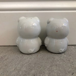 May include: Two white ceramic salt and pepper shakers shaped like pigs. The shakers are facing forward and have a glossy finish.