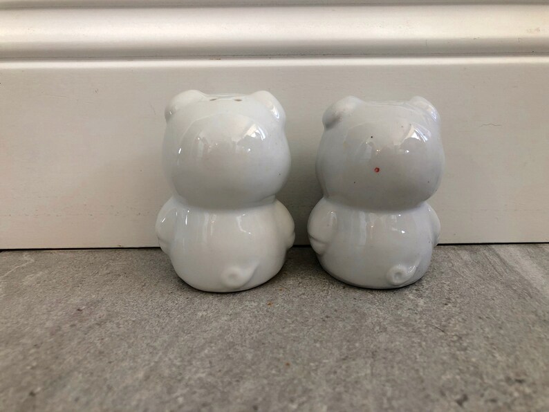May include: Two white ceramic salt and pepper shakers shaped like pigs. The shakers are facing forward and have a glossy finish.