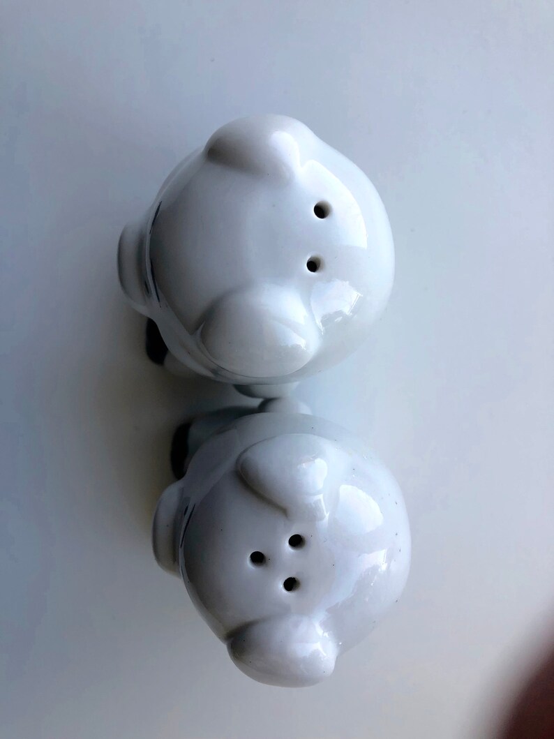 May include: Two white ceramic salt and pepper shakers shaped like pigs. The shakers have holes on top for dispensing salt and pepper.