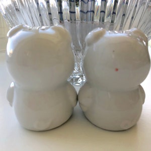 May include: Two white ceramic bear salt and pepper shakers. The bears are facing each other and have a simple, rounded design.