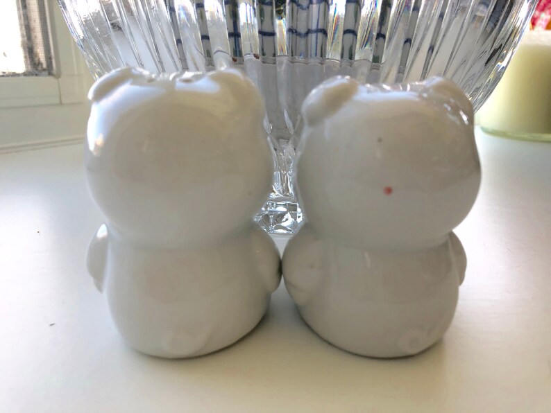 May include: Two white ceramic bear salt and pepper shakers. The bears are facing each other and have a simple, rounded design.