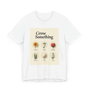 Op de afbeelding: Wit T-shirt met een afbeelding met de tekst "Grow Something". De afbeelding bevat illustraties van een zonnebloem, tomatenplant, rode biet, erwten scheut, aardappel en tuinboon. Het ontwerp is in vintage stijl.