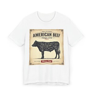 Könnte beinhalten: Weißes T-Shirt mit einem Diagramm der amerikanischen Rindfleisch-Teilstücke. Das Diagramm befindet sich auf einem beigefarbenen Hintergrund mit den Worten "AMERICAN BEEF" und "PRIMAL CUTS DIAGRAM". Eine schwarze Kuhsilhouette befindet sich in der Mitte.