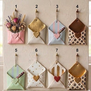 Puede incluir: Una colección de ocho adornos de pared decorativos con forma de sobre. Cada uno tiene un diseño único, incluyendo arreglos florales, detalles dorados, rayas, lunares y estampado de leopardo. Cierres en forma de corazón y están diseñados para colgar en la pared.