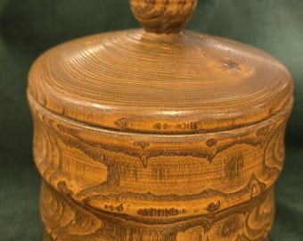 May include: A handcrafted wooden jar with a lid. The jar is a warm brown color with visible wood grain patterns. The lid has a small, rounded knob. The jar's body features a decorative, layered design. The overall aesthetic is rustic and natural.