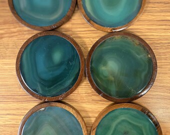 May include: Six round coasters with a teal and green agate design set in a dark wood frame. The coasters are arranged in two rows of three on a light wood surface. The agate pattern varies on each coaster.