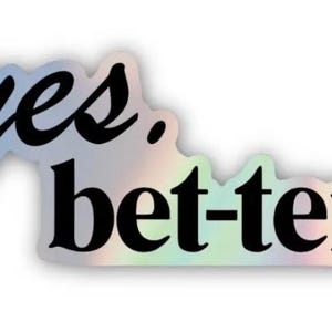 May include: A holographic sticker with the words "yes. bet-ter" in black script. The sticker has a white border and a shimmering, iridescent finish, reflecting a spectrum of colours.
