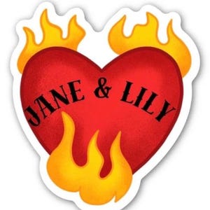 May include: A sticker with a red heart design, displaying the names "JANE & LILY" in black lettering. The heart is encircled by yellow and orange flames. The sticker has a white border.