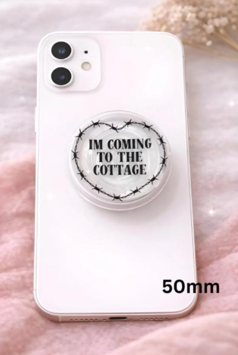 Op de afbeelding: Een witte smartphone met een popsocket bevestigd. De popsokkel heeft een transparante achtergrond met een zwart prikkeldraad hart ontwerp en de tekst "IM COMING TO THE COTTAGE". De popsokkel is 5 cm in diameter.