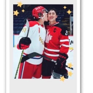 May include: A photograph of two hockey players in red and white jerseys and helmets. One player kisses the other on the cheek. The image is framed with a white border and decorated with star shapes.