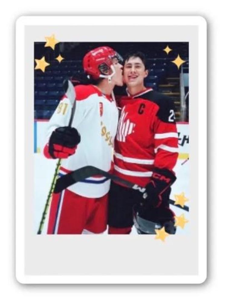 May include: A photograph of two hockey players in red and white jerseys and helmets. One player kisses the other on the cheek. The image is framed with a white border and decorated with star shapes.
