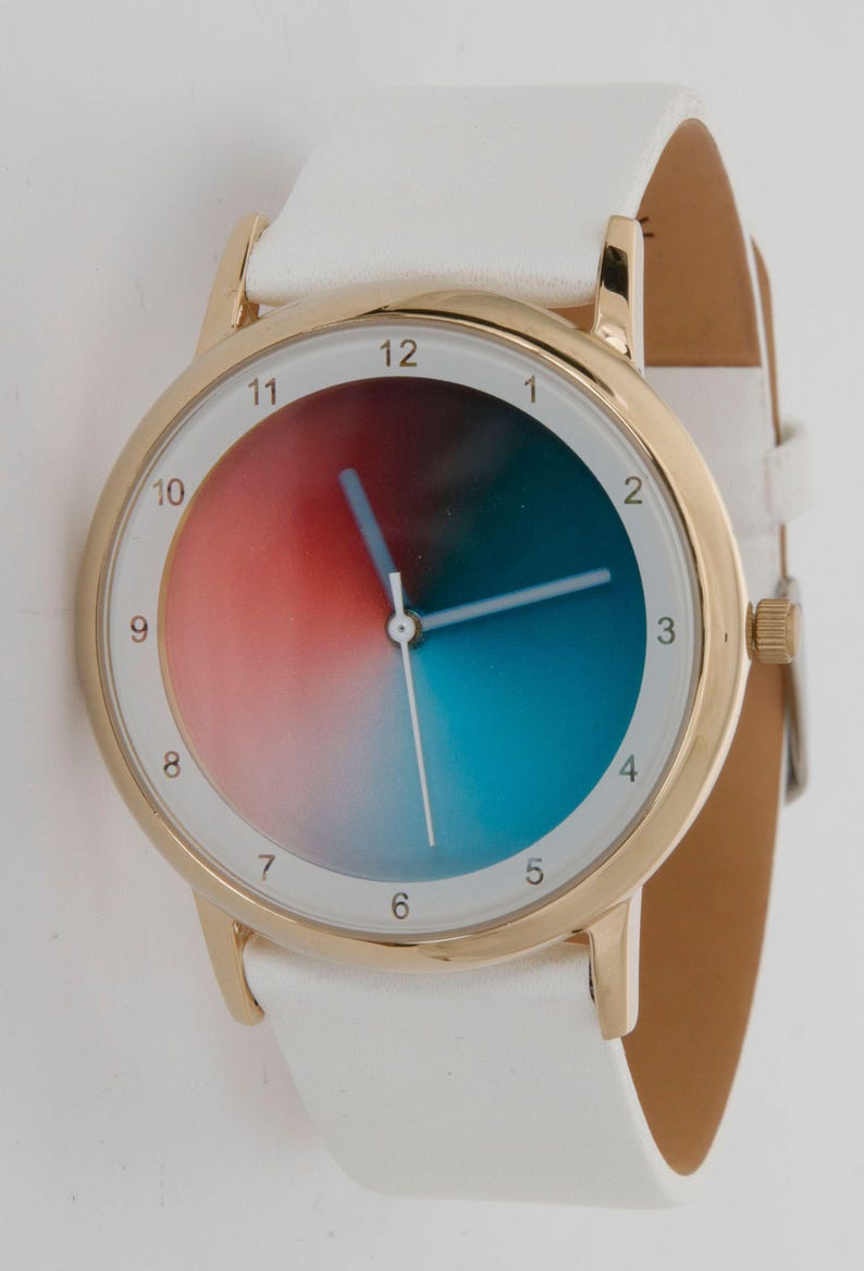 May include: A gold-tone wristwatch with a white leather band. The watch face features a gradient of red, blue, and white. The watch has a gold bezel and white hands. The watch band is white and has a buckle closure.