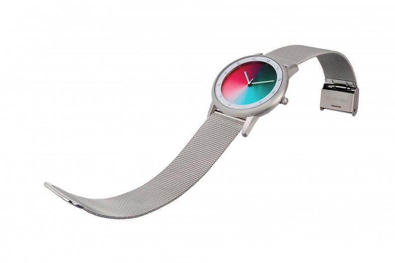 May include: A modern wristwatch with a silver-tone case and a mesh band. The watch face features a gradient of red, green, and teal. The band is unclasped, showing the clasp mechanism. The watch is set against a white background.