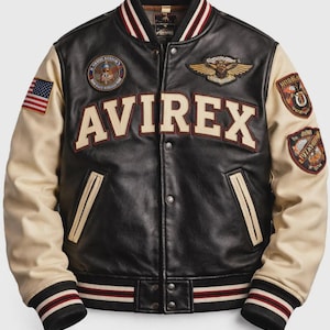 Könnte beinhalten: Eine schwarze Leder-Collegejacke mit cremefarbenen Ärmeln und dem Schriftzug AVIREX auf der Brust. Die Jacke ist mit mehreren gestickten Aufnähern, einem gestreiften Rippstrickkragen, Bündchen und Saum sowie einer kleinen amerikanischen Flagge am Ärmel versehen.