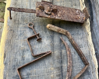 May include: A selection of old, rusty metal hardware components. The image shows a latch, a clamp, and several bent metal rods. These items are displayed on a weathered wooden surface, highlighting their aged appearance and historical value.