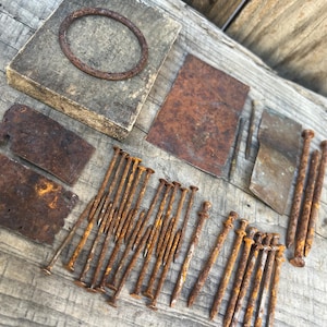 Puede incluir: Una colección de herrajes metálicos oxidados y desgastados que incluye un anillo circular, varias placas planas rectangulares y un gran surtido de clavos de diversos tamaños. Todos los elementos presentan una pátina marrón oxidada.