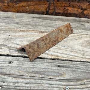 Op de afbeelding: Een roestige metalen hoekbeugel met een ruw, verweerd oppervlak.