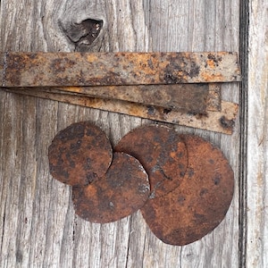 May include: A collection of weathered metal components featuring three rectangular strips and four circular discs. Each piece displays a heavy, textured brown and orange rust patina across its entire surface, indicating significant oxidation.