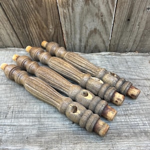 May include: Four matching wooden furniture legs with a turned, spindle-style design. Each leg features a natural brown wood grain, a central fluted section, and rounded decorative rings. The ends of each leg are tapered for attachment purposes.