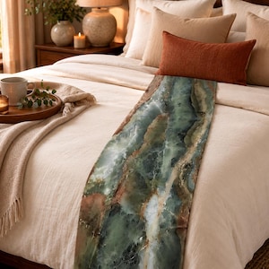 May include: A bed runner featuring a marbled pattern in shades of sage green, deep forest green, and white with subtle brown veining. The runner is draped over a cream-colored duvet cover on a bed with several pillows in neutral and rust tones.