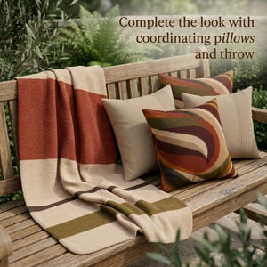 May include: A throw blanket and three pillows on a wooden bench. The blanket features horizontal stripes in rust, beige, and olive green. One pillow has a wavy rust, beige, and olive pattern, while two are solid beige. Text reads: Complete the look with coordinating pillows and throw.