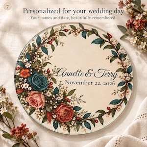May include: A round glass plaque featuring a floral wreath border with teal, pink, and red roses and green leaves. The center displays the text Annette & Terry and the date November 22, 2026, in a dark script and serif font.