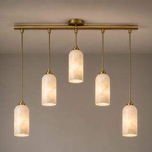 Puede incluir: Una lámpara de techo lineal con una barra horizontal de latón y cinco varillas verticales de distintas longitudes. Cada varilla sostiene una pantalla cilíndrica de vidrio blanco veteado y translúcido que emite un brillo cálido.
