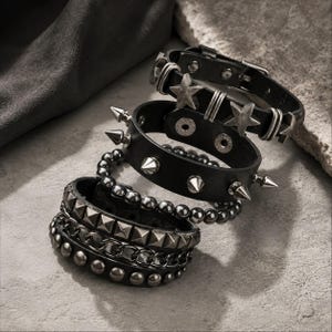 May include: A set of four black bracelets featuring various metallic embellishments including silver-toned stars, conical spikes, smooth spherical beads, pyramid studs, and a chain link design, all secured with snap buttons or adjustable buckle closures.