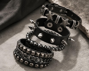 Puede incluir: Un conjunto de cuatro pulseras negras con diversos adornos metálicos, incluyendo estrellas plateadas, púas cónicas, cuentas esféricas lisas, tachuelas piramidales y un diseño de cadena, aseguradas con botones a presión o hebillas.