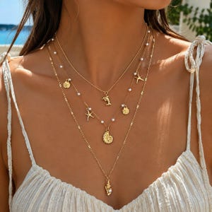 May include: A layered gold-tone necklace set featuring three delicate chains adorned with small white beads. The pendants include a dolphin, a starfish, a spiral seashell, and a conch shell, creating a cohesive nautical-themed jewellery accessory.