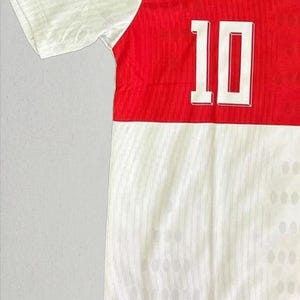 May include: A white and red athletic jersey with the number 10 in white. The jersey has a white upper section and a red lower section. The text "sporysupply" is at the bottom.