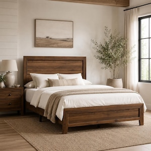 Op de afbeelding: Een houten bedframe met een hoofdbord, nachtkastje en een tapijt in neutrale tinten. Het bed is opgemaakt met wit beddengoed en een beige sprei. Een lamp staat op het nachtkastje. Een schilderij hangt aan de muur boven het bed.