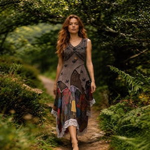 May include: A sleeveless patchwork dress with a V-neck and a layered skirt. The dress has a brown bodice with embroidered details and a colourful, patterned skirt. White lace trim edges the hemline. The dress is worn outdoors on a path.
