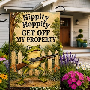 May include: A rectangular garden flag featuring a green frog holding a shotgun in front of a wooden fence. The text "Hippity Hoppity GET OFF MY PROPERTY" is printed in black letters at the top. The flag is displayed on a black metal stand.