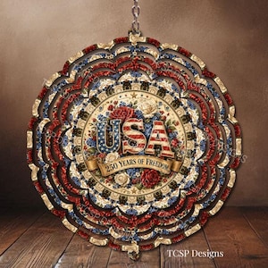 May include: A round, decorative ornament with a patriotic theme. The design features the word "USA" in red, white, and blue, surrounded by floral patterns and the text "250 Years of Freedom". The ornament is suspended by a chain.