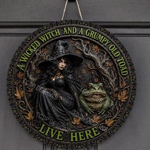 Puede incluir: Un letrero de pared circular con una ilustración en relieve de una bruja con sombrero y vestido negro sentada junto a un sapo verde grande. El texto A WICKED WITCH AND A GRUMPY OLD TOAD LIVE HERE está impreso en verde alrededor del borde.