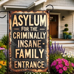 May include: A rectangular garden flag featuring a distressed black background with a rusted metal border. The text reads ASYLUM FOR THE CRIMINALLY INSANE- FAMILY ENTRANCE in bold, gold-colored, sans-serif capital letters. The flag hangs on a metal stand.