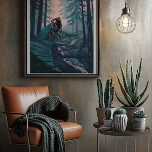 May include: A framed print of a mountain biker riding through a forest. The print is in a dark blue and green color scheme with a pink sky in the background. The print is hanging on a wall in a room with a leather chair, a side table, and plants.