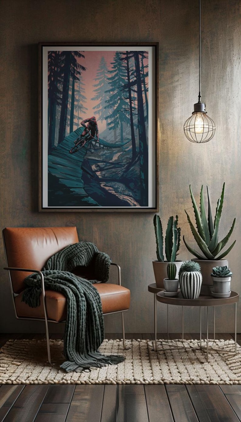 May include: A framed print of a mountain biker riding through a forest. The print is in a dark blue and green color scheme with a pink sky in the background. The print is hanging on a wall in a room with a leather chair, a side table, and plants.