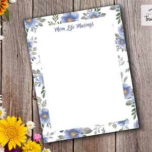Puede incluir: Una hoja de papelería blanca con un borde floral azul y el texto "Mom Life Musings". La hoja está rodeada por un fondo de madera y flores coloridas, incluyendo margaritas y girasoles. La papelería es de "Thula Mae Stationery & More".