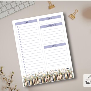 Puede incluir: Un bloc de notas blanco con un diseño floral y de libros en la parte inferior. El bloc de notas tiene secciones etiquetadas como "To Do", "Date", "Important" y "Notes" en color lila claro. El bloc de notas está sobre una superficie beige claro con un teclado y material de oficina.